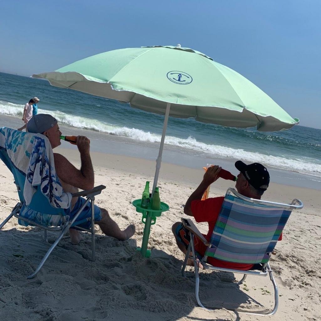 two men on the beach sitting under the Anchor Works beach umbrella